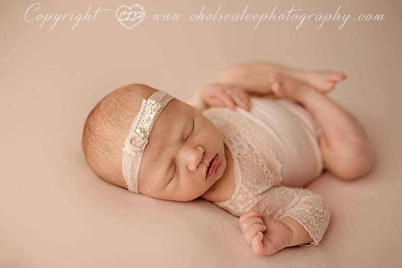 baby girl sleeping on back in adorable pink romper and headband